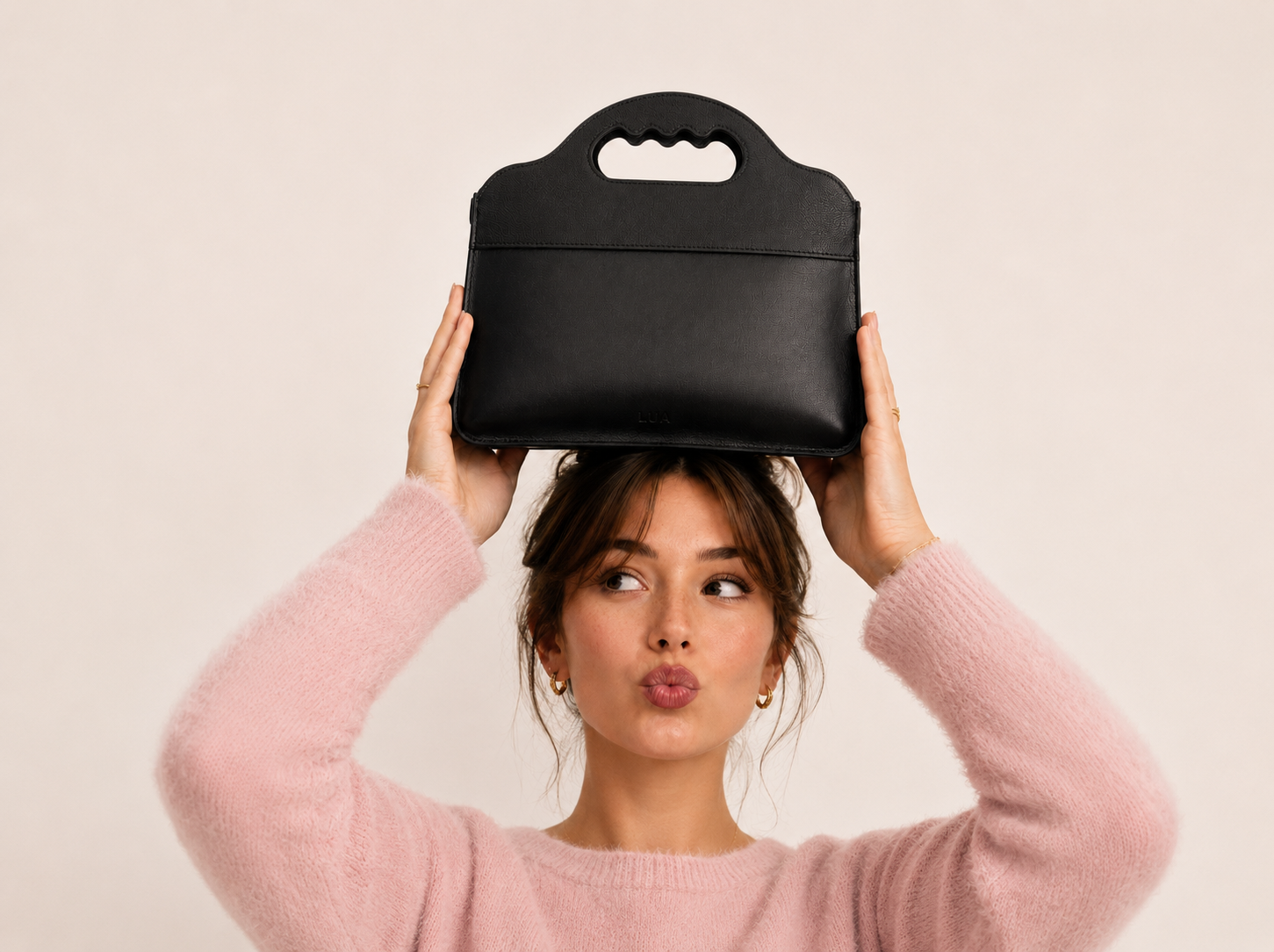 Femme en pull rose tenant le sac Lua au-dessus de sa tête